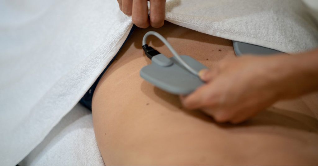 Bioelectric energy session setup Alt text: Grey electrode pad applied to hip area during BMT, with skin partly covered by a towel. Description: Close-up of a practitioner attaching an electrode pad to a person’s lower abdomen for bioelectric meridian therapy.