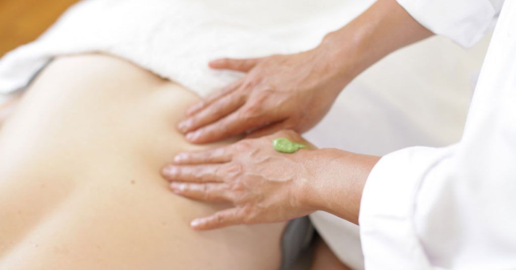 Bioelectric Meridian Therapy session in progress Description: Practitioner applies green lotion while performing BMT on a person’s bare back, towel draped, face down. Alt text: Close-up of BMT therapist’s hands pressing gently on a client’s back with green gel, white towel from waist up.