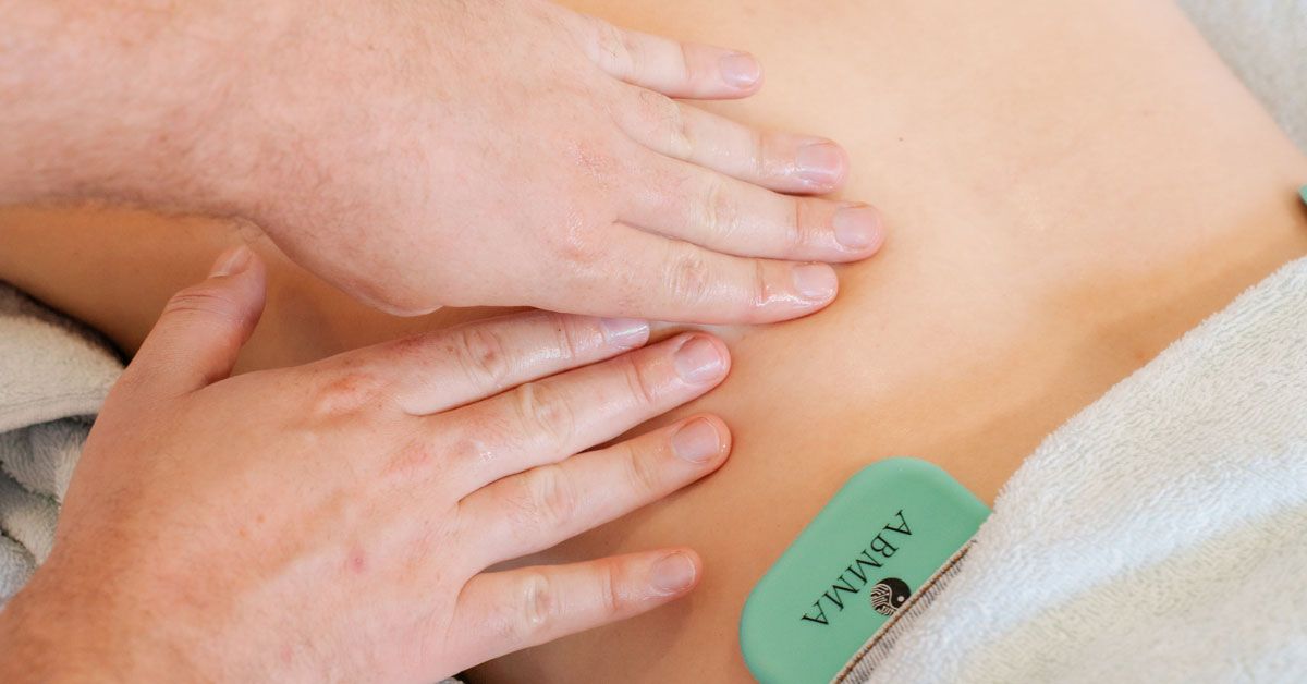 Paul and Anne’s hands performing BMT on a bare back, with a bioelectric device nearby. Recipient draped in white towel, content. Bioelectric Meridian Therapy session: hands massaging back near device, recipient relaxed under towel. Hands delivering bioelectric meridian massage; therapy tool at edge; peaceful client partly covered with towel.