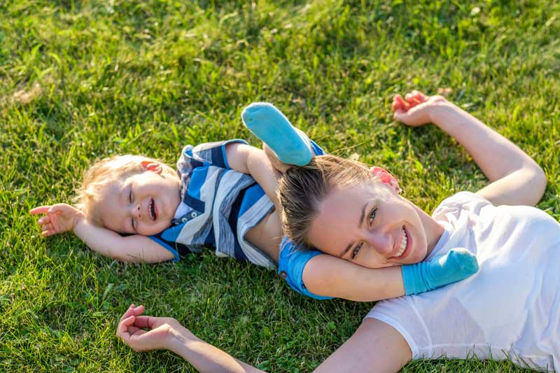Experience Renewal with Bioelectric Meridian Therapy Alt text: Smiling woman and child lying on lush grass, enjoying a joyful, uplifting moment inspired by BMT’s restorative approach. Description: An outdoor scene of laughter and connection between a woman and child, capturing wellbeing achieved through Bioelectric Meridian Therapy.