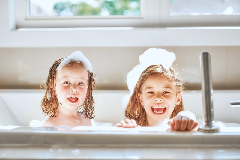 Joyful bath time with bubbles, sunlight, and laughter Description: Two children enjoy a bubbly bath, their smiles reflecting the positive vibes of Bioelectric Meridian Therapy sessions. Alt text: Happy children sit in a sunlit tub with foam and soap suds on their heads, evoking the joy of BMT healing energy.