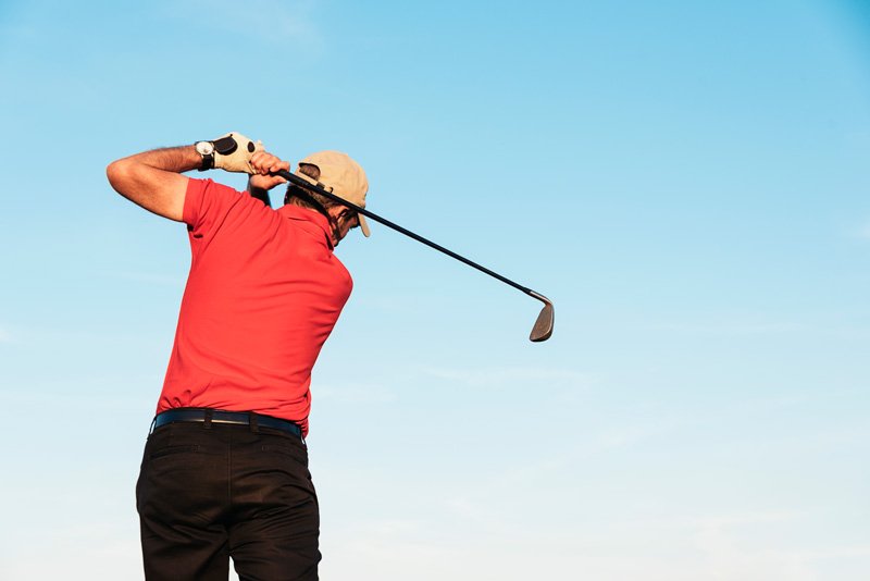 Golfer Powered by Bioelectric Meridian Therapy Alt Text: Golfer in red shirt and black trousers swings club outdoors, benefiting from Bioelectric Meridian Therapy. Description: Energised golfer in red and black, swinging on a sunny course, enhanced by BMT for improved wellbeing and performance.