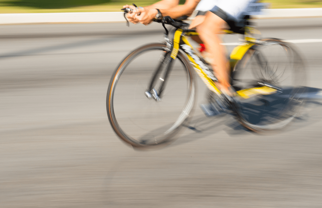 Cyclist speeds down street on black and yellow bike, muscles engaged, motion blur highlights Bioelectric Meridian Therapy benefits. Description: Blurred image shows focused cyclist training intensely, visually echoing BMT’s activation of muscle energy and overall vitality. Title: Road cyclist in motion symbolising the energising effects of Bioelectric Meridian Therapy.
