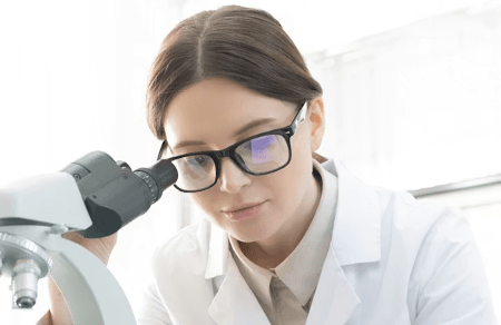 A woman in a lab coat studies samples using a microscope, exploring the science behind Bioelectric Meridian Therapy. Description: Focused female scientist with glasses examines slides under a microscope, connecting findings to BMT research. Title: Laboratory work advancing Bioelectric Meridian Therapy.